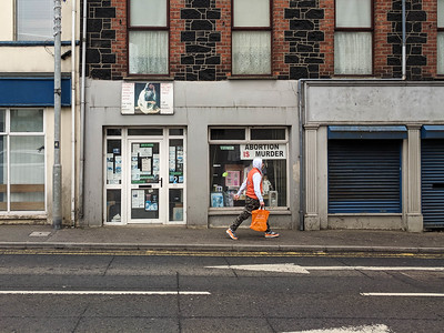 Person walks down a street in Northern Ireland with a sign in the shop window that says "Abortion is murder"